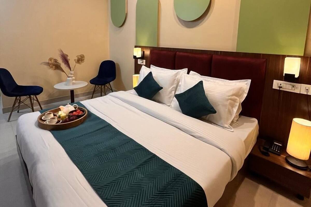 A hotel room with a bed, a bedside table with a lamp, a small round table with chairs, and a ceiling fan.