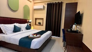 A hotel room with a large bed, a desk, a ceiling fan, and an air conditioning unit. - Pink Guava  (Gurugram)
