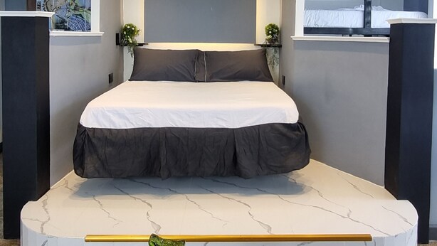 Habitación de hotel moderna con cama central, luces empotradas en el techo, un detalle de mármol y una pequeña escultura verde.