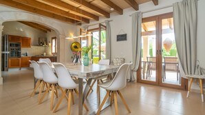 Ein geräumiger Essbereich mit einem Holztisch und weißen Stühlen, eine Küche mit Holzausstattung und einem modernen Herd sowie ein großes Fenster mit Vorhängen.