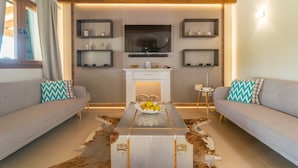 Ein modernes Wohnzimmer mit zwei Sofas, einem Couchtisch mit Obstschale, einem Kamin und einem an der Wand befestigten Fernseher.
