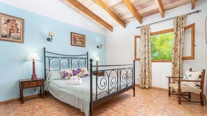 Ein Schlafzimmer mit einem Metallbettgestell, einem Nachttisch aus Holz, einem Stuhl und einem Fenster mit Vorhängen.