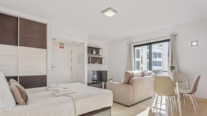 Moderni hotellihuone, jossa on sänky, sohva, ruokapöytä ja televisio.