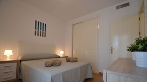 Een keurig opgemaakt slaapkamer met een bed, twee bedlampen, een kunstwerk aan de muur, een gesloten deur en een potplant.