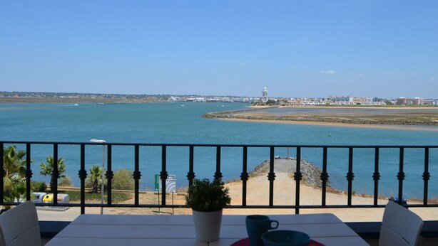 Uitzicht op zee vanaf een balkon met een tafel, stoelen, een potplant en een leuning.