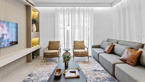 A modern living room with a flat-screen TV, two leather armchairs, a sofa with leather cushions, a coffee table, and a chandelier.