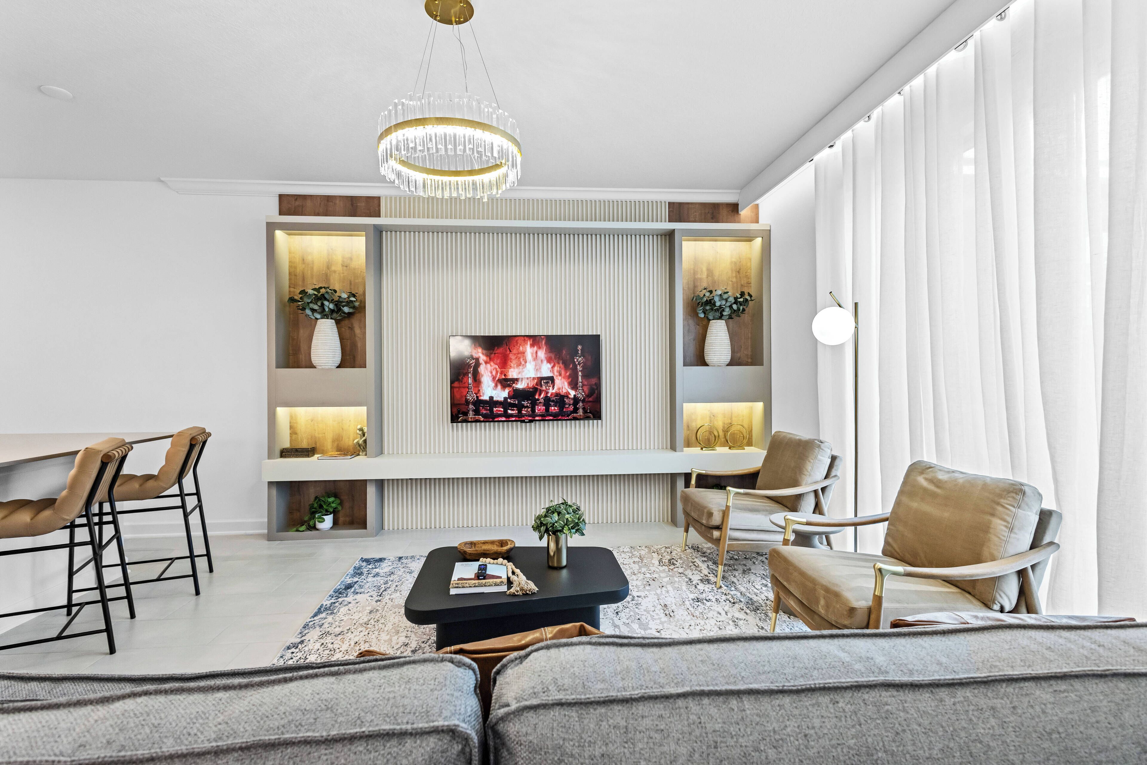 Ein modernes Wohnzimmer mit Flachbildfernseher, bequemen Sitzmöglichkeiten, einem Couchtisch und dekorativen Pflanzen.