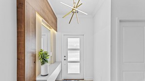 A hallway with a white door, a wooden accent wall, a white bench, a plant, and a ceiling light fixture.