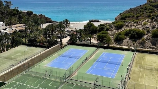 Ein Tennisplatzkomplex mit mehreren Plätzen, umgeben von Grünflächen und mit Blick auf Strand und Meer.
