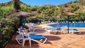 Ein Poolbereich mit Liegestühlen und Sonnenschirmen, umgeben von Grünflächen und Hügeln.