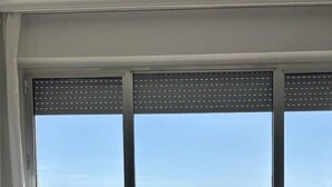 Ein Zimmer mit großem Fenster und Meerblick, ein weißer Konsolentisch mit Spielzeugauto und Lautsprecher, sowie Ausblick auf eine felsige Küstenlinie.