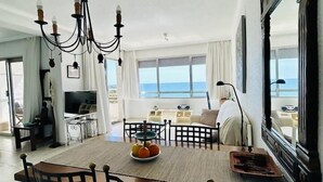 Ein geräumiges Wohnzimmer mit einem großen Esstisch, einem Kronleuchter und Blick auf das Meer.