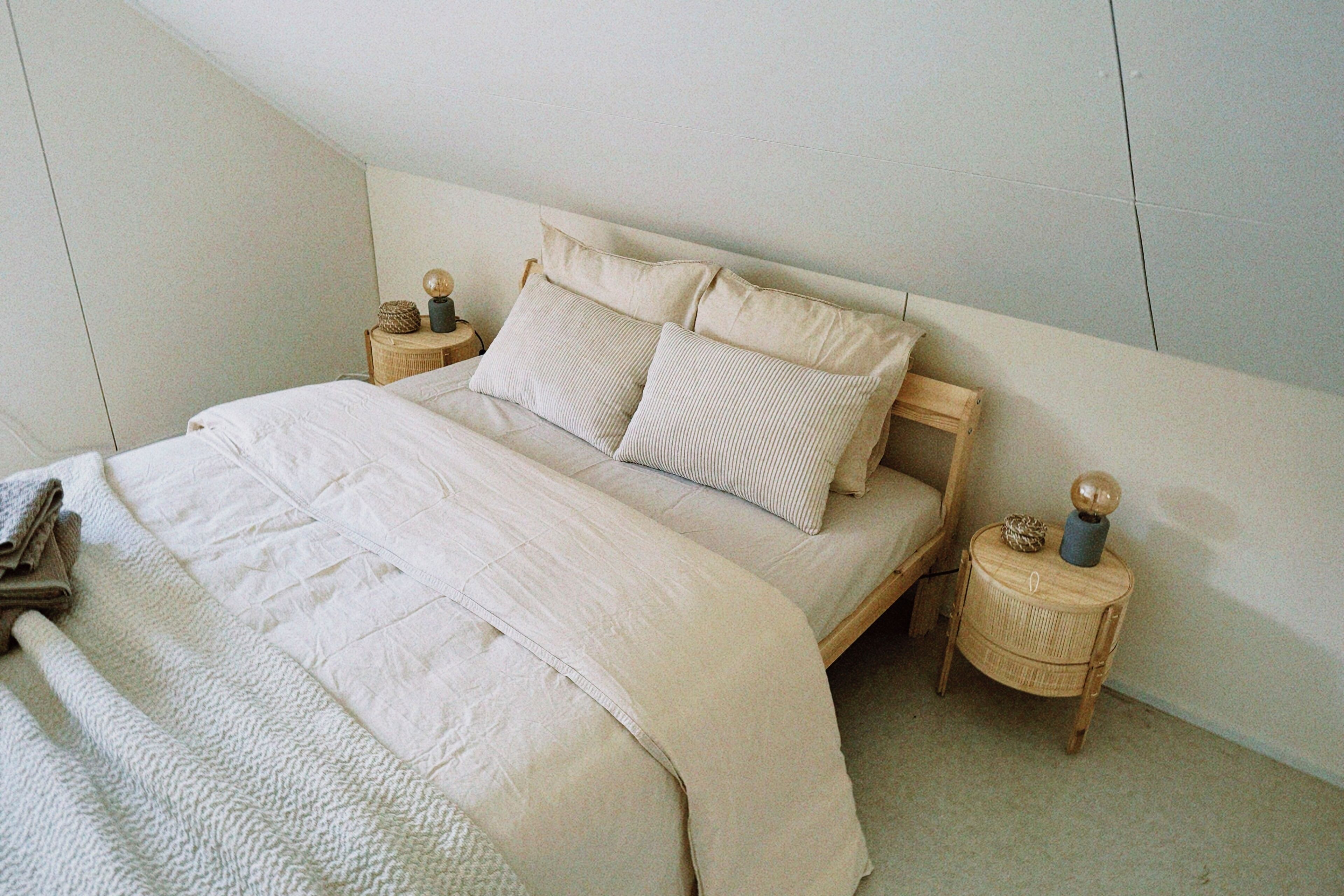 A neatly made bed with a quilt and pillows, a bedside table with a lamp, and a small round table with decorative items.