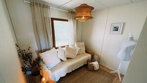 Et hyggeligt værelse med en sofa, et lille bord med en plante, en hængende lampe og et billede i ramme på væggen.