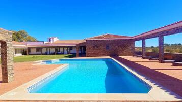 Una piscina con un motivo a rilievo geometrico, circondata da una terrazza con pilastri in pietra e un'area salotto coperta.