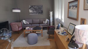 A living room with a grey sofa, a coffee table, a grey ottoman, a TV, and a lamp.