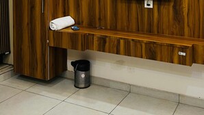 A modern room with a wooden wall panel, a mounted air conditioner, a flat-screen TV, a bench, and a trash bin. - Rana Ji Haveli (Najibabad)