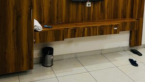 A modern hotel room with a wooden panel wall, a flat-screen TV mounted on the wall, a built-in air conditioning unit, a small trash bin, and a pair of slippers on the floor. - Rana Ji Haveli (Najibabad)