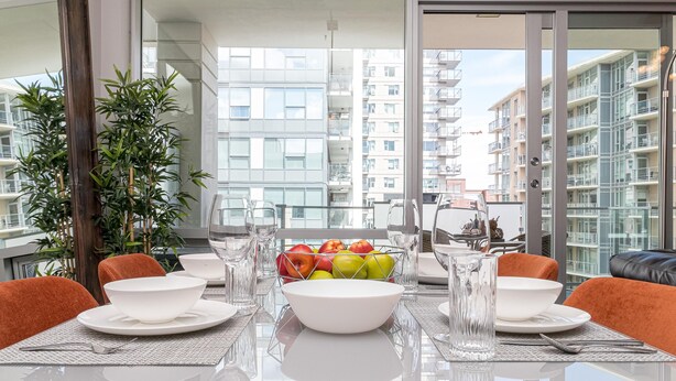 Ett modernt matområde med ett glasbord, vita tallrikar och en skål med frukt.