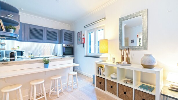 A modern kitchen with a central island, bar stools, built-in shelves, and a large mirror.
