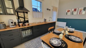 Una cocina moderna con armarios oscuros, una encimera de madera y un comedor con una mesa preparada para dos.