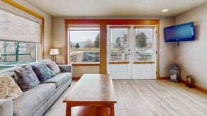 A living room with a sofa, a wooden table, a TV, and a view of a balcony with a railing.