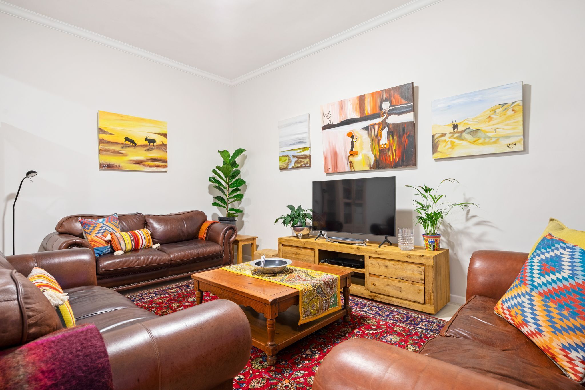 A living room with a brown leather sofa, a wooden coffee table, and a flat-screen TV on a wooden stand.