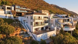 A modern multi-story residential building with balconies, a swimming pool, and a hillside backdrop.