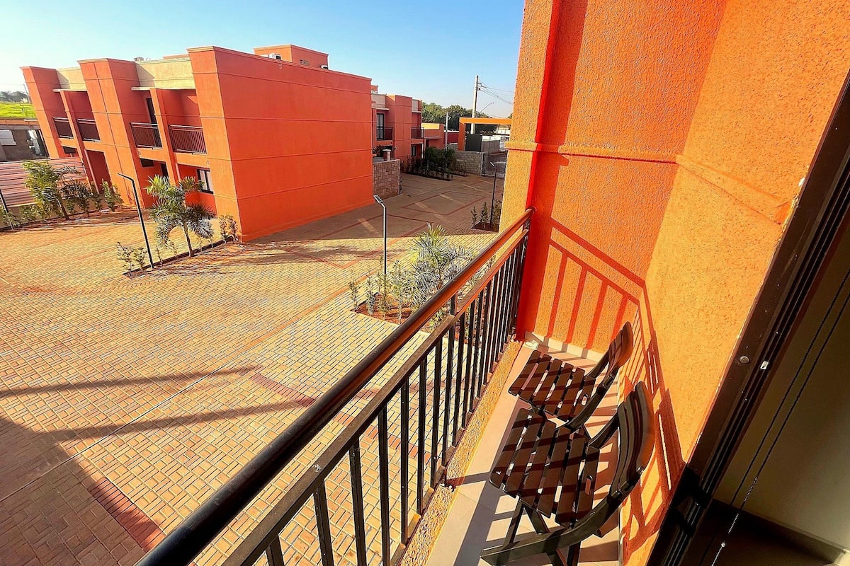 A balcony with a metal railing overlooking a paved area with small plants and a building in the background.