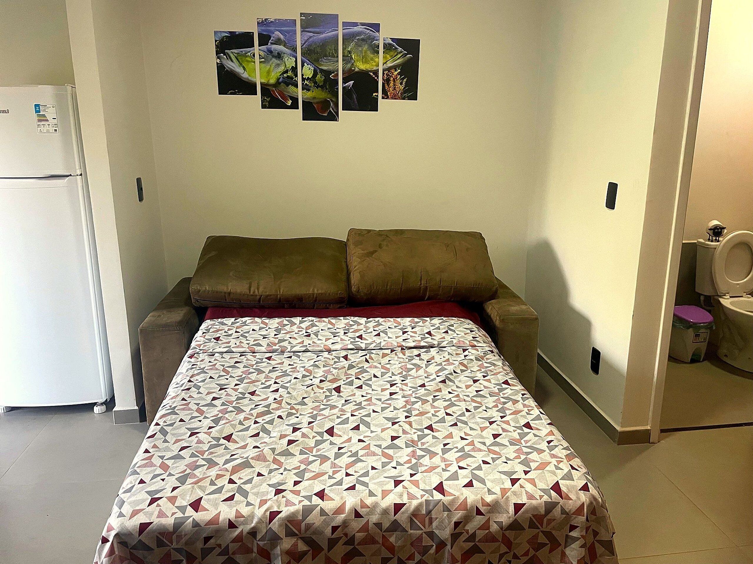 Ein kleiner, kompakter Raum mit Bett, Sofa, Kühlschrank und Toilette.