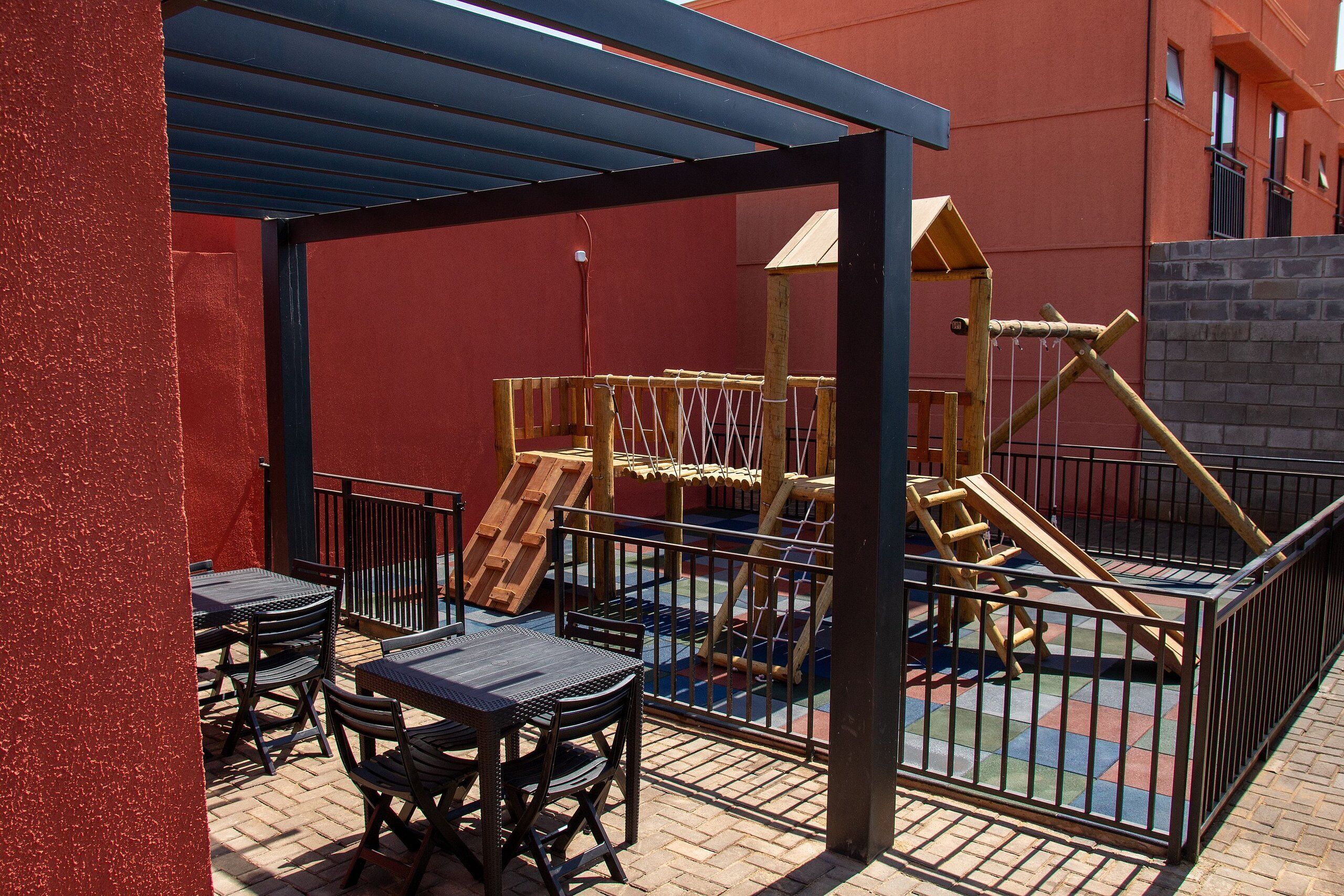 An outdoor patio with a play area, including a wooden play structure and a fenced play zone.