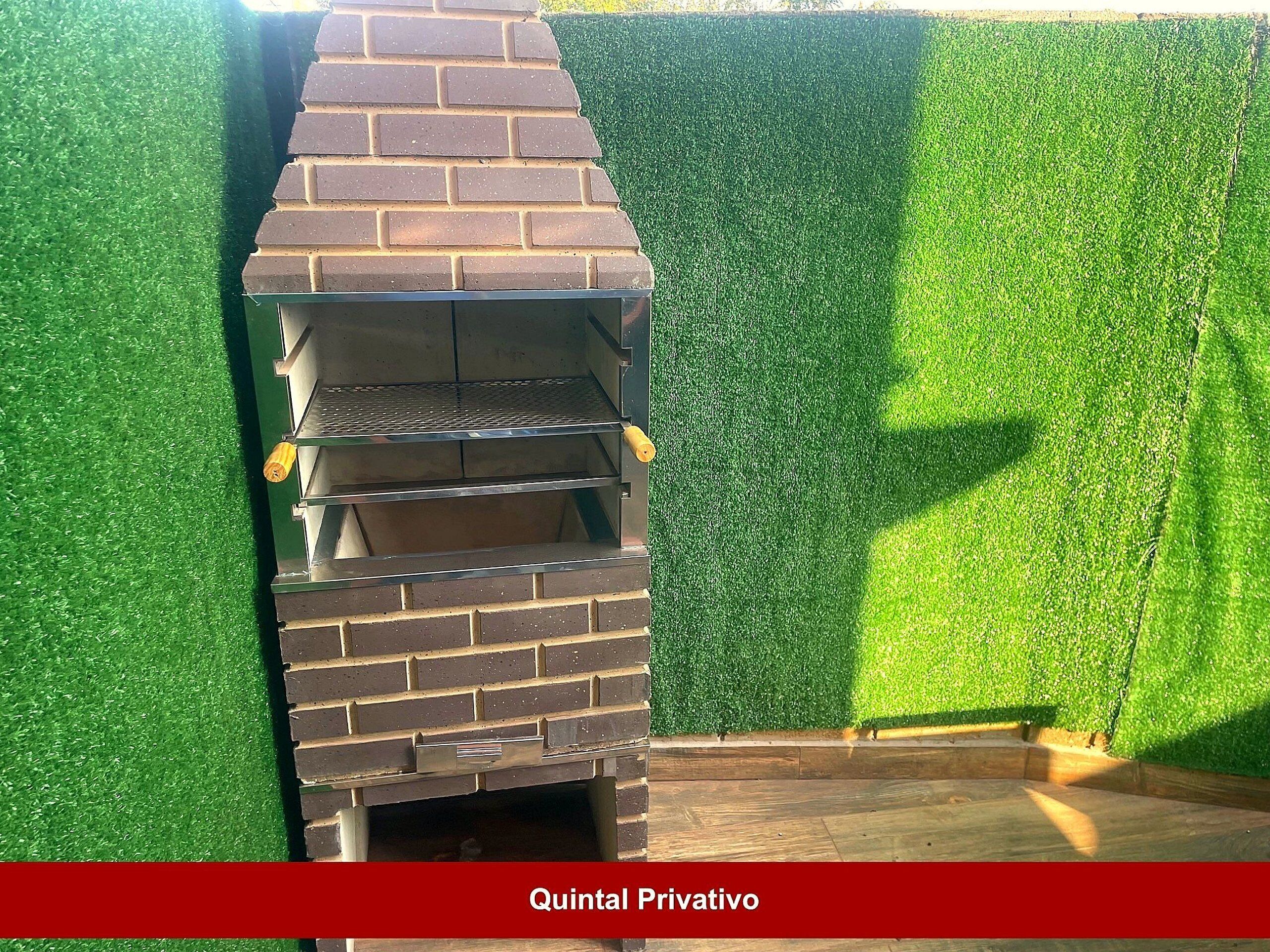 Uma churrasqueira de tijolos ao ar livre com chaminé, em frente a um muro verde artificial.