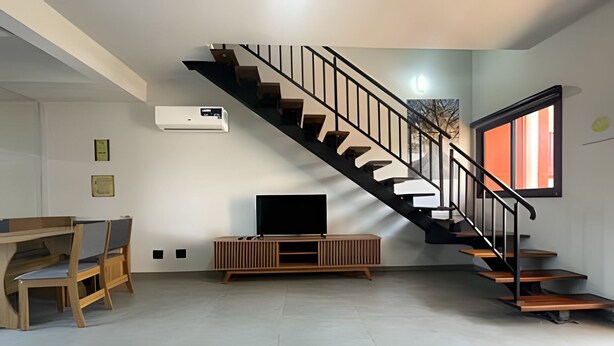 A modern living room with a staircase, a flat-screen TV, and a built-in air conditioner.