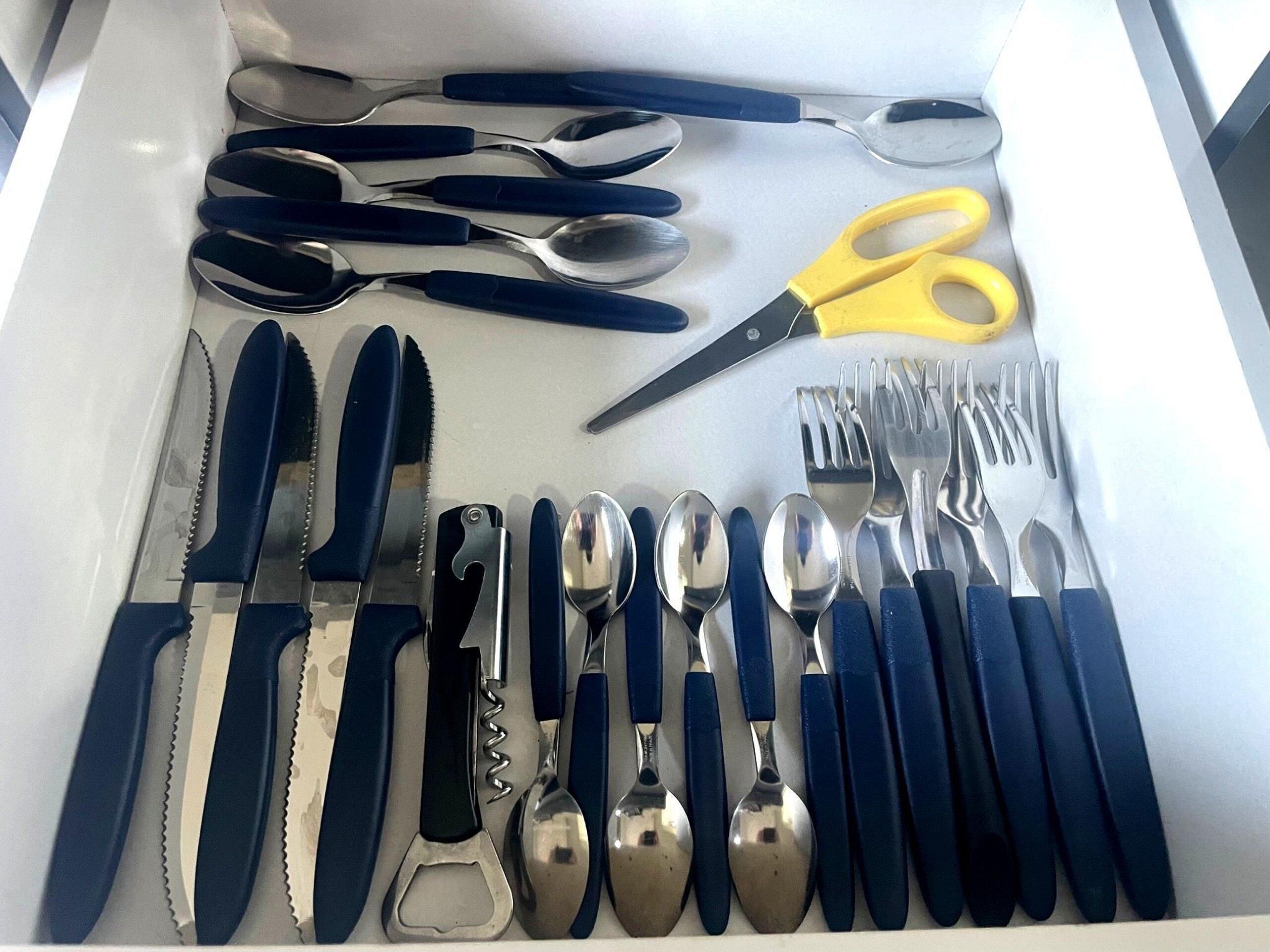 A drawer containing various utensils including knives, forks, spoons, and a pair of scissors.