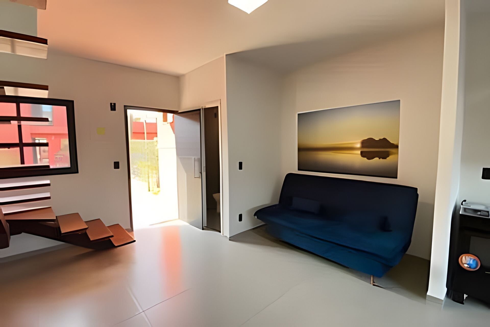 A modern living room with a blue sofa, a staircase, and a large painting on the wall.