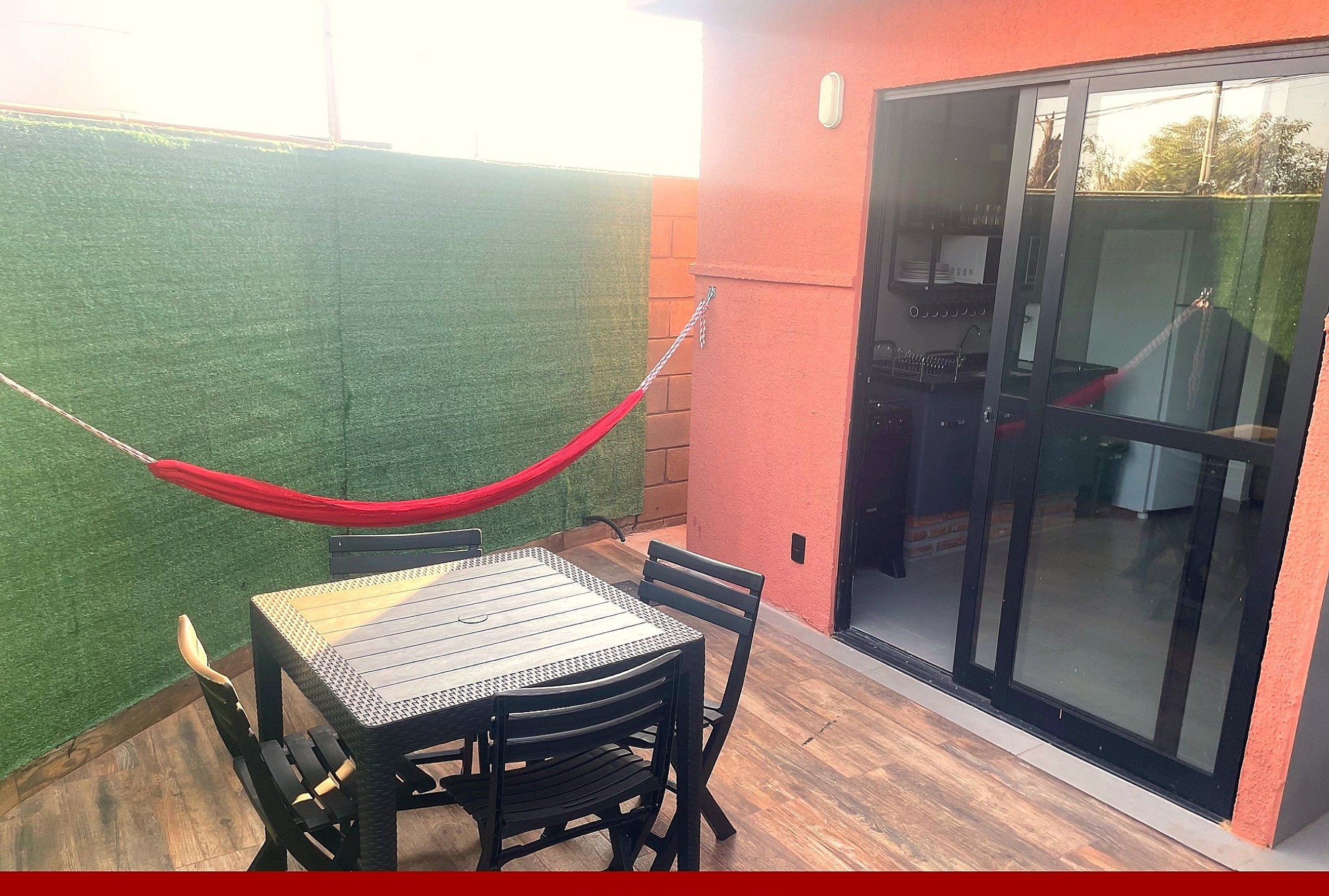 A patio with a table and chairs, a red hammock, and a sliding glass door leading to an indoor area.