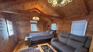 A cozy cabin with a wooden interior, a bed, a sofa, and a small table with a picture frame.
