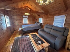 A cozy cabin with a wooden interior, a bed, a sofa, and a small table with a picture frame.