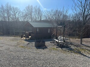 Ein rustikales Blockhaus mit Metalldach, umgeben von einer Schotterfläche und kahl stehenden Bäumen.