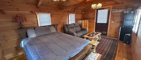 A cozy cabin room with a large bed, a chair, a small table, and a kitchenette.