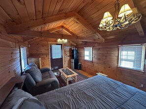 A cozy cabin interior with a large bed, a sofa, a small table, and a chandelier.