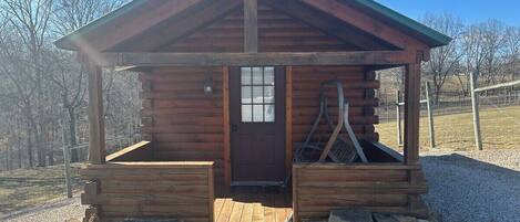 A small wooden cabin with a pitched roof, a front door, and a porch area.