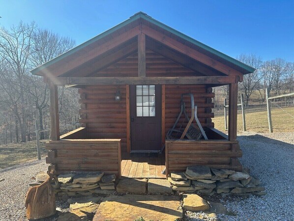 A small wooden cabin with a pitched roof, a front door, and a porch area.