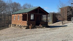 A small log cabin with a green roof, a porch, and a stone foundation.