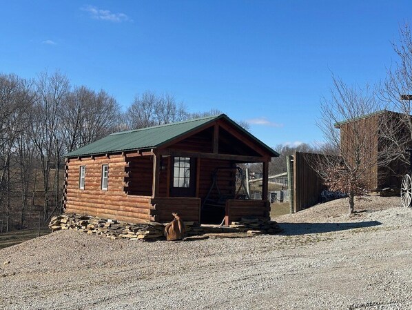 A small log cabin with a green roof, a porch, and a stone foundation.