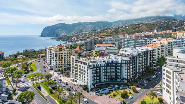 A coastal cityscape with modern buildings, a curved road, and a view of the sea.