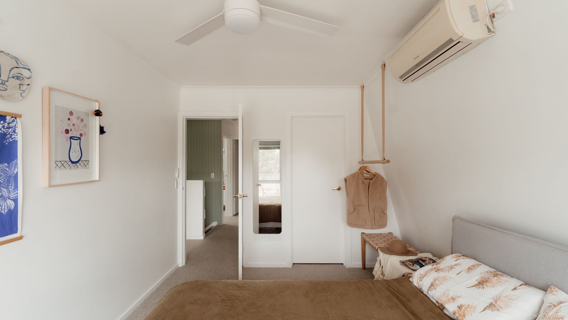 Una camera da letto con un letto, una sedia a dondolo, un condizionatore d'aria a parete e una porta che dà su un'altra stanza.