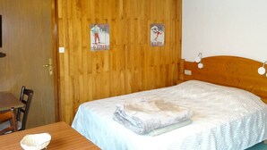 A wooden-paneled room with a bed, a table, and two posters on the wall.