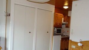 A bedroom with a bed, a wardrobe, and a kitchenette with a microwave and refrigerator. - Central Studio for 2 in Les Gets - Balcony, Free WiFi, Linens Included (Les Gets)