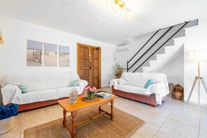 Uma sala de estar com dois sofás brancos, uma mesa de centro de madeira, uma escada e uma porta.